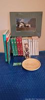 Overview of the Anne of Green Gables books, videos, framed photo, ceramic statue, and plate arranged on a blue surface.