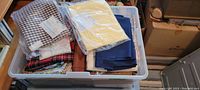 Top view of bin filled with assorted fabric pieces including gingham, plaid, solid, and wrapped fabrics, placed in plastic storage container.