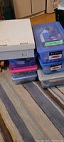 Seven boxes stacked on a carpeted floor including plastic storage bins and a cardboard box containing Christmas crafting materials.