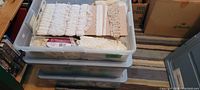 Top view of plastic bin showing various lace trimming pieces, some rolled on spools, others wrapped on cardboard, all in cream/white tones.