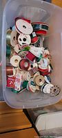 Top-down view of a large plastic bin filled with multiple rolls of ribbons and bow making materials.
