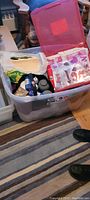 Photo of large plastic storage bin with pink lid containing crafting supplies including tulle, decorations, and wooden signs