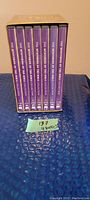 Photo showing the full boxed set of 7 DVDs standing upright on a blue surface with the spine labels visible.