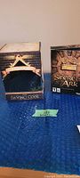 Two boxed sets: The Davinci Code DVD gift set and Secrets of the Ark PC video game box are displayed side by side on a blue surface.