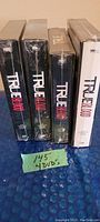 Four sealed DVD box sets of True Blood seasons 1 through 4 standing upright together.