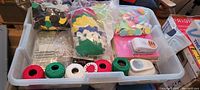 Top view photo showing assembled foam craft supplies including foam shapes, yarn spools, punch tools, googly eyes and other crafting accessories arranged in a plastic storage bin