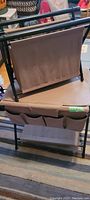 Overall view of two folding taupe canvas art bins, one with pockets and one plain, supported by black metal folding frames, in good condition.