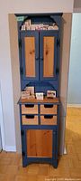Full view of closed narrow pine cabinet showing blue painted frame and natural wood panel doors, small drawers in center.
