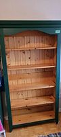 Front view of the wooden Shaker style bookcase showing four adjustable natural wood shelves and green painted frame with plank back paneling.