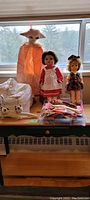 Photo showing two vintage dolls, assorted doll clothes, laundry bag with panda prints, and panda hangers arranged on window ledge.