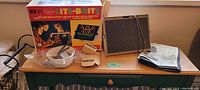 Photo showing the entire set on a table including the Lite Brite peg board, original box, peg bowl, peg organizer, tweezers, and instruction manual.