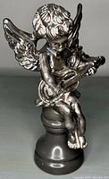 Front view of sterling silver cherub figurine holding a guitar, sitting on a black base.