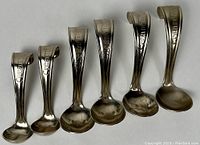 Group of six curved cream spoons, two small and four large, with visible patent text on handles.