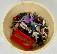 Top view of bin filled with various small vintage toys including a Cracker Jack box, purple toy machines, miniature figures, and a silver trophy cup