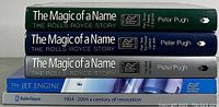 Stacked view of the five books showing three volumes of 'The Magic of a Name: The Rolls-Royce Story' by Peter Pugh in green, blue, and silver hardcover, 'The Jet Engine' softcover, and 'Rolls-Royce 1904-2004 a century of innovation' softcover.