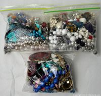 Three clear sandwich bags filled with assorted vintage costume jewelry items including bead necklaces, clip-on earrings, and bracelets in a variety of colors