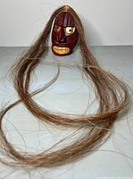 Front view of red-stained wooden mask with long horsehair draped forward