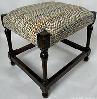 Side angle view of walnut footstool showing tapered legs with faceted detailing and knit patterned cushioned seat.