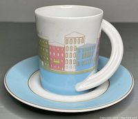 Side view of porcelain espresso cup showing colorful cityscape design on cup and light blue band on saucer with gold trim