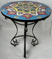 Front view of round mosaic stone top table with colorful intricate pattern and black wrought iron base.
