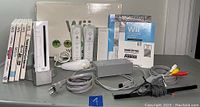 Wide shot of Nintendo Wii console with original box, two remotes, nunchuck, power adapter, sensor bar, cables, and manuals.
