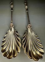 Pair of spoons laid side by side showing scalloped shell bowls and decorative handles