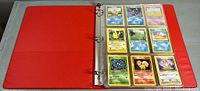 Open red three-ring binder showing nine classic Pokemon cards including Pikachu, Pichu, Abra, Bulbasaur, and others, all in plastic card sleeves.