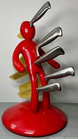 Front view of red humanoid knife block on round base with five knives inserted