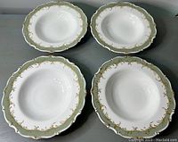Four Royal Doulton soup bowls displayed with scalloped edges and a green border decorated with gold scrolls.