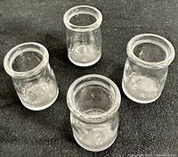 Four clear small glass creamer bottles on black cloth background showing size and condition.