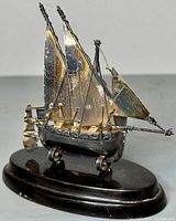 Front angle view of the sterling silver Maltese sailing junk ship figurine mounted on an oval lacquered wood base.
