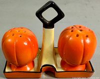 Close-up photo of the pumpkin-shaped salt and pepper shakers on the matching tray, showing the orange glaze and the black handle.