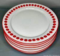 Stack of eight white pottery bread plates with red polka dot designs and red rim edges.