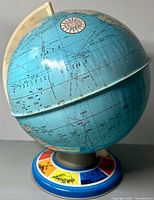 Front and side angle showing the blue tin globe with Pacific Ocean centered and part of North America, mounted on colorful base with landmark illustrations.