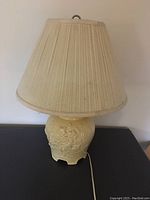 Lamp with visible cream ceramic floral base and pleated fabric shade.
