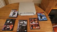 PlayStation 2 console with six game cases arranged around it on a wooden table. Games shown: NHL 2K7, Smugglers Run, Tom Clancy's Splinter Cell, DJ Vendetta, and two others.