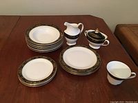 Wide view of dish set showing various plates, a cream pitcher, sugar bowl with lid, and a teacup on a wooden table