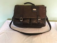 Front view of the dark brown leather briefcase with top handle and shoulder strap laid out.