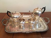Full set of silver plated tea and coffee vessels with tray, shown from front, displaying matching engraved floral patterns.