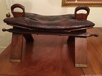 Front view of stool frame with leather cushion in place and carved handles