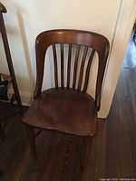 Front view of one solid wood chair showing curved backrest with vertical slats and contoured seat.