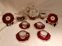 Full view of tea set arranged with teapot, sugar bowl, creamer, four cups and saucers, and two extra gold-trimmed plates on stands