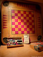 Photo of wooden Carrom board with rounded corners, checkerboard pattern, game pieces box, instruction booklet, and original box.