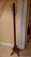 Full front view of tall wooden coat rack standing on carpeted floor near wall.
