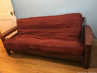 Full frontal view of the wood futon with red mattress showing the mattress and frame, highlighting the storage arms and overall structure.