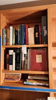 Photo showing entire wooden bookshelf with three shelves filled with assorted vintage books. Top shelf features a mix of hardcover books including the red-covered 1938 edition of Charles Dickens A Christmas Carol in plastic slipcover.