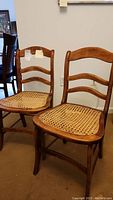 Photo of two vintage wooden chairs with cane seats, showing full front view of both and their curved backrest with hoop relief crossbars.