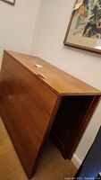 Side view of solid wood gate leg drop leaf dining table with one drop leaf folded down against wall.
