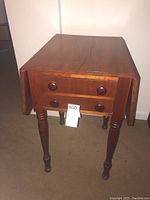 Front view of the wooden side table with drop leaf sides folded down, showing two drawers and round wooden knobs.