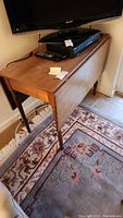 Wooden drop leaf table folded with turned spindle legs and rectangular top with TV and remote on top.